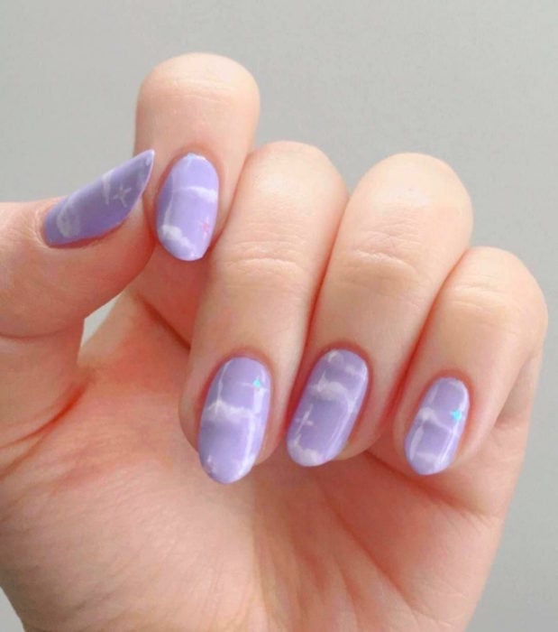 Manicura con diseño de cielo y nubes; uñas cortas en forma de almendra pintadas con esmalte lila morado