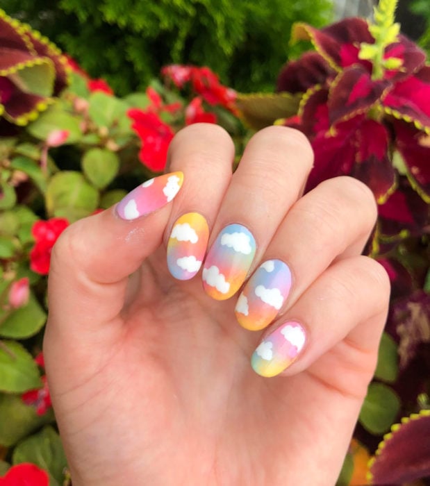 Manicura con diseño de cielo y nubes; uñas cortas en forma de almendra pintadas con esmalte de colores arcoíris, amarillo, rosa, morado, verde, azul degradado