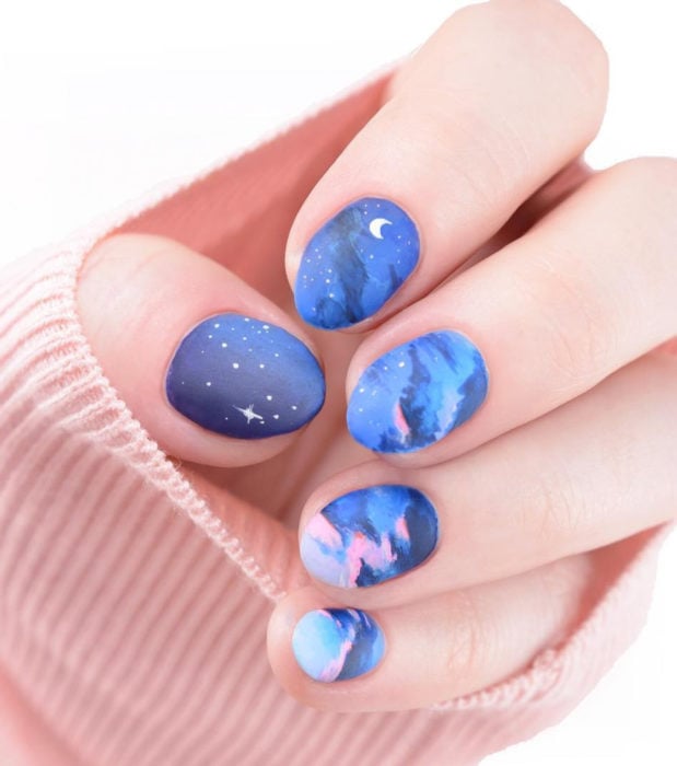 Manicura con diseño de cielo y nubes; uñas pintadas con esmalte azul y rosa formando estrellas y luna