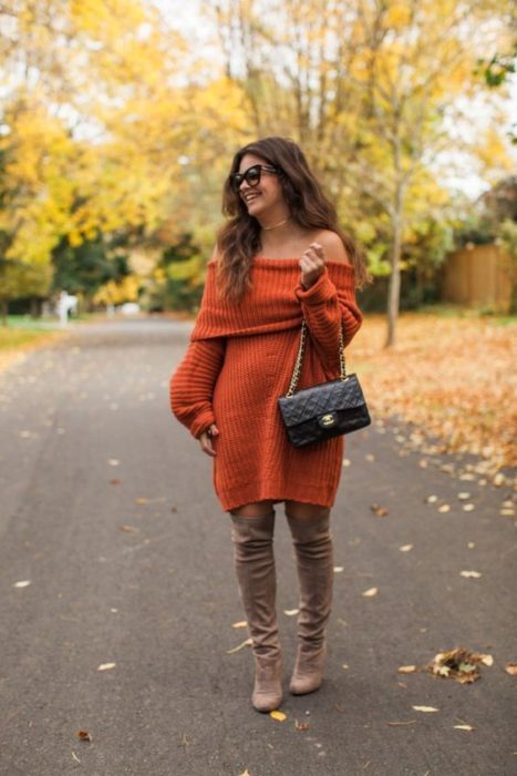 Chica de cabello castaño largo con vestido naranja largo y botas cafés