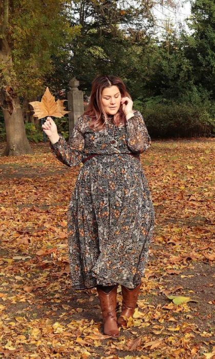 Chica plus size con vestido de chifón largo de flores posando en hojas amarillas caídas