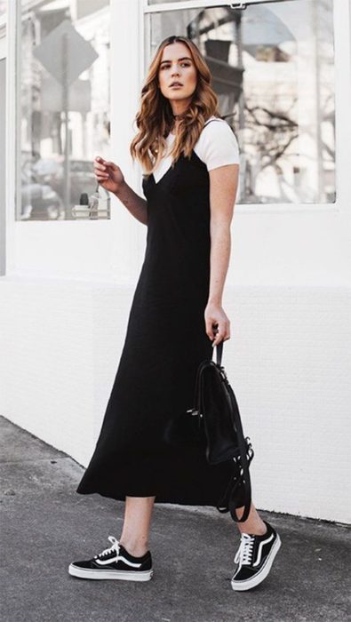 Chica rubia delgada con cabello suelto viste vestido largo y negro con blusa blanca por debajo