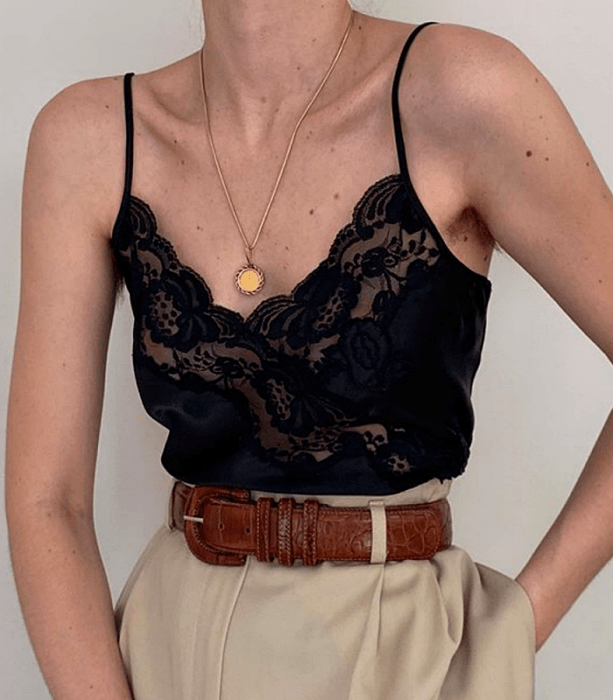 blusa negra de tirantes con encaje negro cruzado escote en v, cinturón café de piel, pantalones beige de vestir a la cintura y collar de oro con medalla