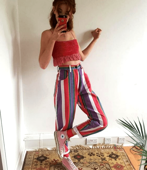 chica pelirroja usando pantalones de rayas azules, rosas y blancos con crop top de tirantes rosa intenso y converse rosas