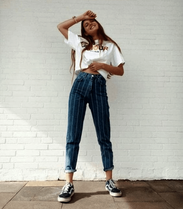 chica de cabello castaño usando una camiseta blanca con jeans de rayas y tenis negros