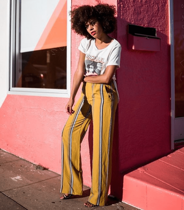 chica morena usando una camiseta blanca con estampado y pantalones de rayas amarillos con linea azul y blanca