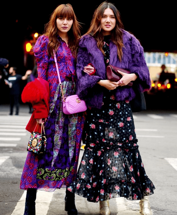 chica de cabello castaño usando un vestido morado estampado con flores rojas y formas tribales, botines negros de terciopelo, bolso rosa y bolso negro con lunares de colores, abrigo rojo. chica de cabello castaño usando un vestido negro con estampado de rosas, botines dorados, bolso morado de mano