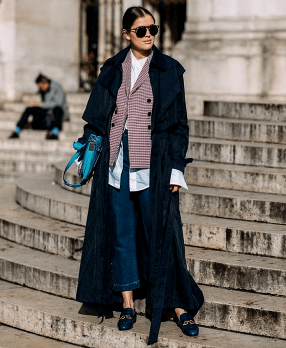 chica de cabello castaño usando una camisa de vestir blanca, saco rojo de cuadros, abrigo azul marino largo, jeans, loafers azul marino y bolso azul de mano