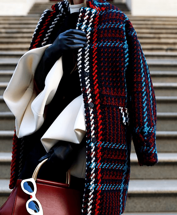 chica usando una blusa blanca, suéter negro, guantes de cuero, abrigo largo de cuadros azul, rojo, blanco y celeste, bolso rojo de mano y lentes de sol blancos