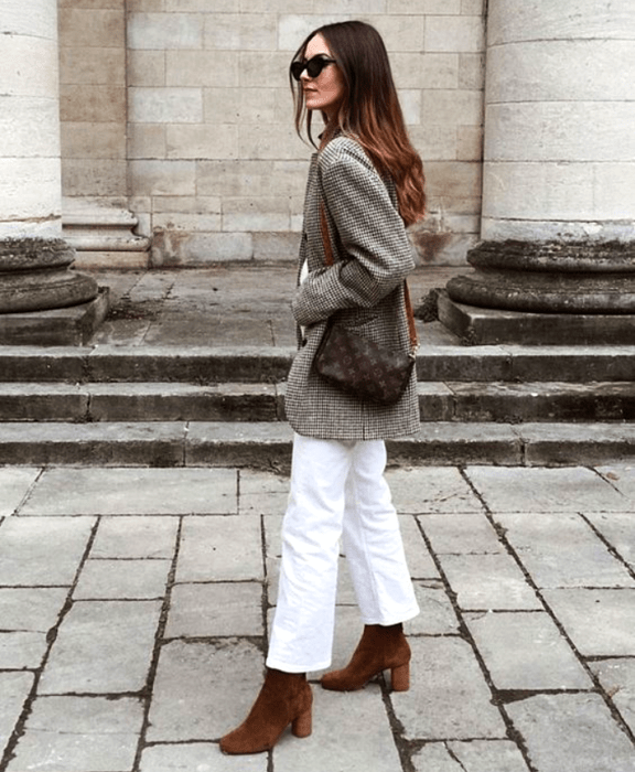 chica de cabello castaño largo con lentes de sol, saco abrigo gris, pantalón blanco, bolso café y botines de terciopelo cafés