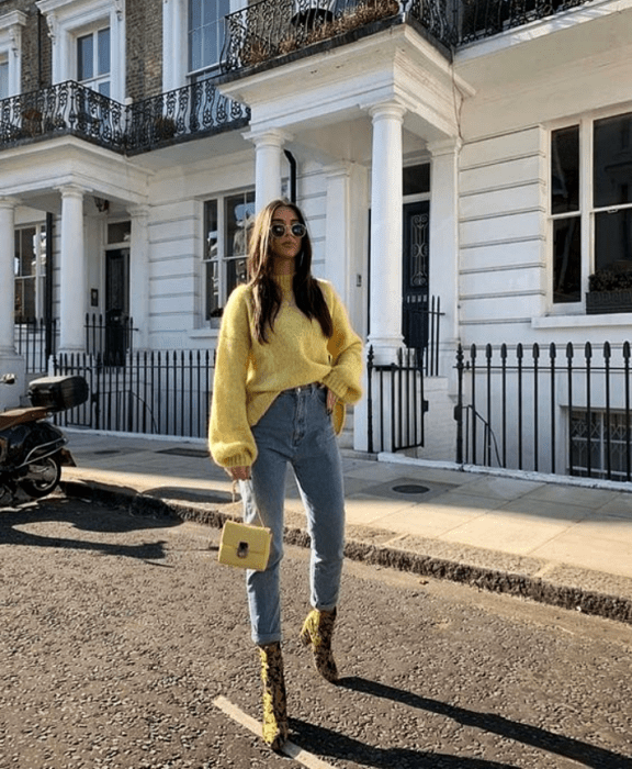 chica de cabello castaño largo usando lentes de sol, suéter amarillo, minibolso amarillo, skinny jeans y botines amarillos con negro