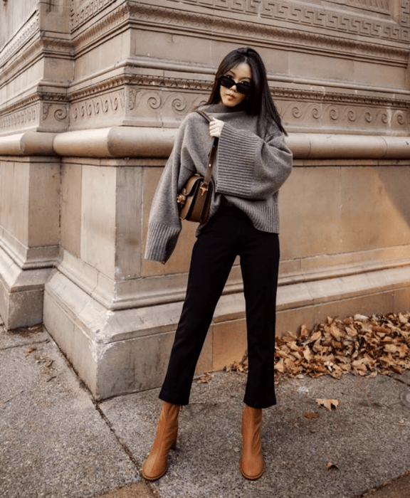 chica de cabello castaño usando lentes de sol, sudadera gris, pantalón negro, bolso estampado, botines de color café claro de cuero