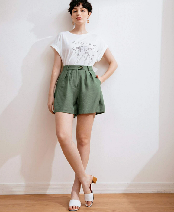 chica de cabello corto negro usando una camiseta blanca de manga corta, paperbag shorts verdes y sandalias de piso blancas