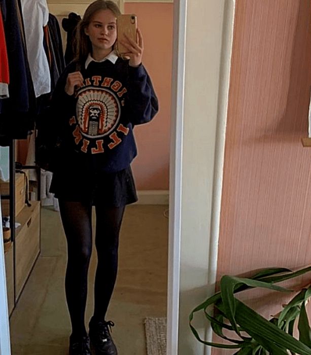 chica rubia usando una sudadera con estampado, minifalda negra, medias negras y tenis negros deportivos