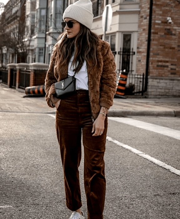 chica de cabello castaño usando lentes de sol, gorro beanie beige claro, top blanco, abrigo teddy café, pantalones de pana cafés, tenis blancos y bolso mini negro