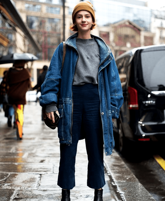 chica pelirroja usando un beanie gorro café, sudadera gris, chamarra de mezclilla, pantalones de mezclilla tipo culotte y botines negros