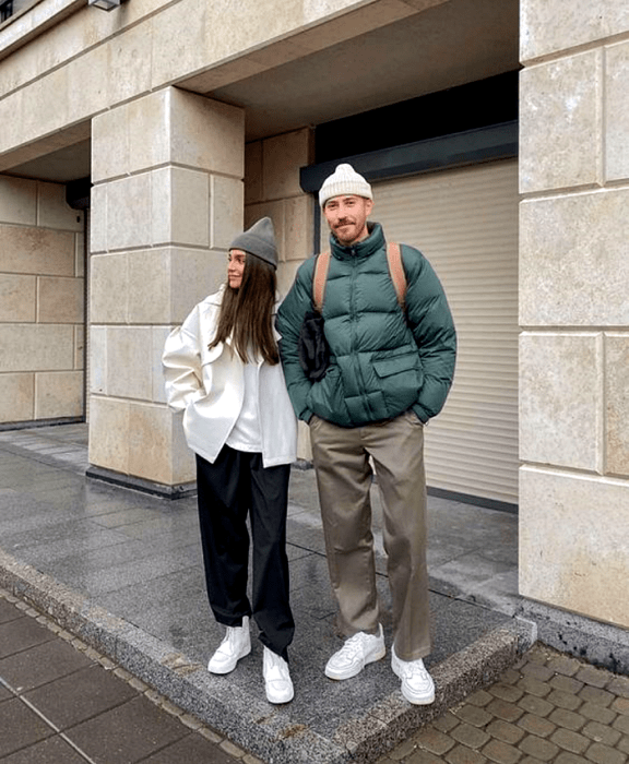 pareja de novios, la chica de cabello castaño usando un beanie gorro verde, chamarra blanca, top blanco, pantalones azul marino, tenis blancos y el chico usando un beanie gorro blanco, chamarra puffer jacket verde, pantalones grises y tenis blancos