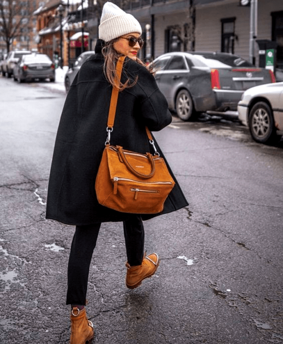 chica de cabello claro usando un beanie gorro blanco, abrigo negro, bolso grande café, skinny jeans negros y botines cafés