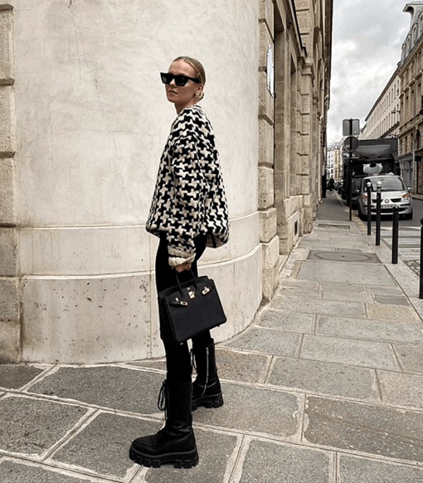 chica rubia con lentes de sol usando una sudadera de cuadros blanca con negro, leggings negros, botas de cuero negras y bolso mini de cuero negro