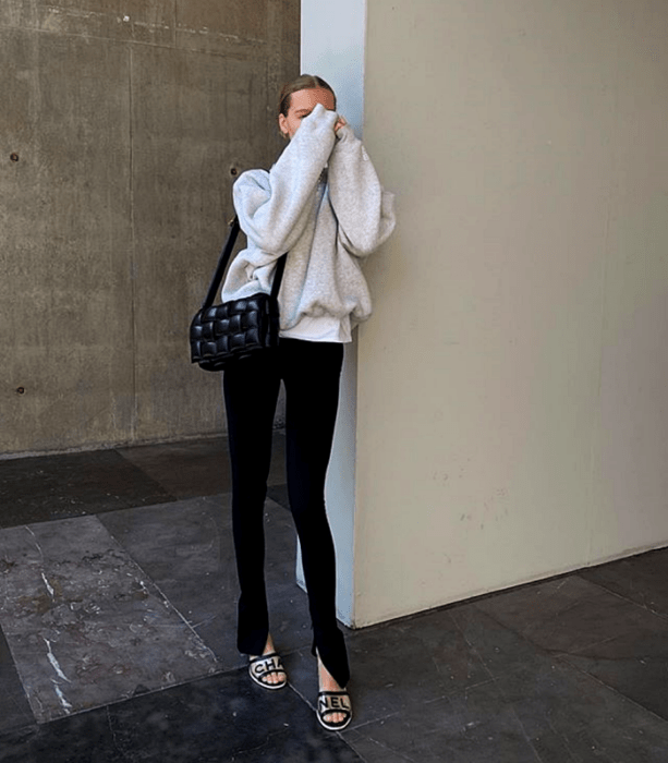 chica rubia usando una sudadera blanca, top blanco, bolso negro de mano, leggings negros y sandalias blancas de tacón