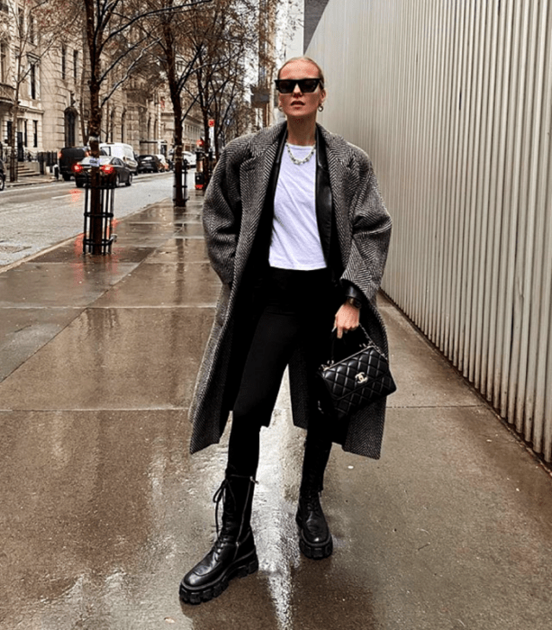 chica rubia usando lentes de sol, top blanco, chaqueta de cuero, abrigo largo de cuadros, leggings negros y botines negros de plataforma y bolso negro