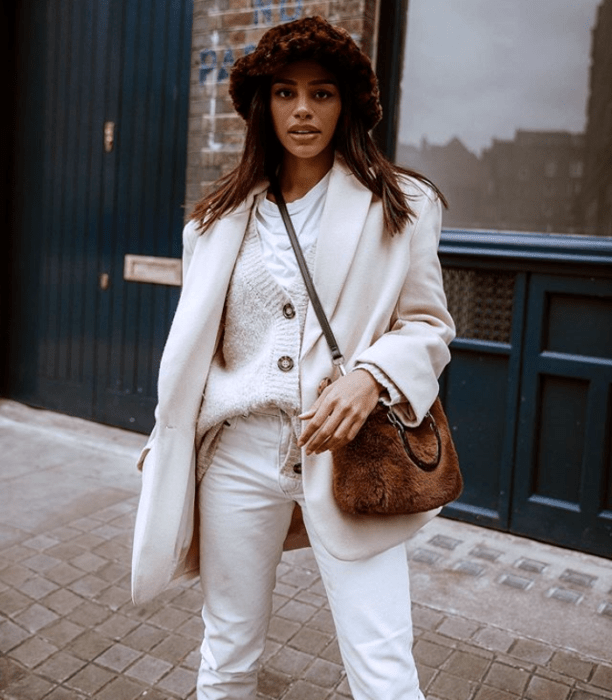 chica morena usando un bucket hat de piel con estampado de animal print, abrigo beige, suéter blanco y pantalones blancos