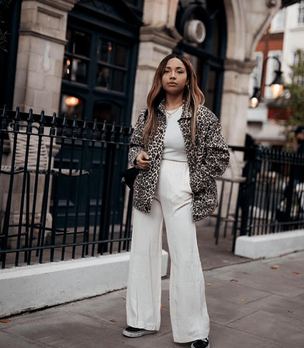 chica morena usando un abrigo de animal print, top blanco, pantalones acampanados de vestir blancos 