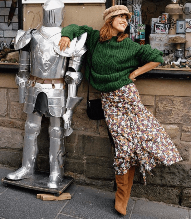 chica de cabello castaño usando un gorro beige, suéter verde, falda de flores larga y botas de piel cafés con tacón