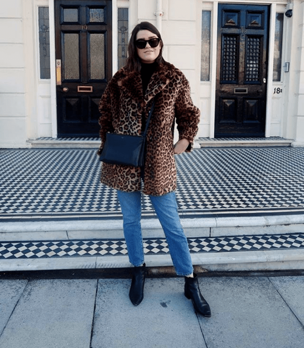 chica de cabello corto negro usando lentes de sol, abrigo de peluche de animal print, skinny jeans, botines negros de cuero negros, bolso de mano negro