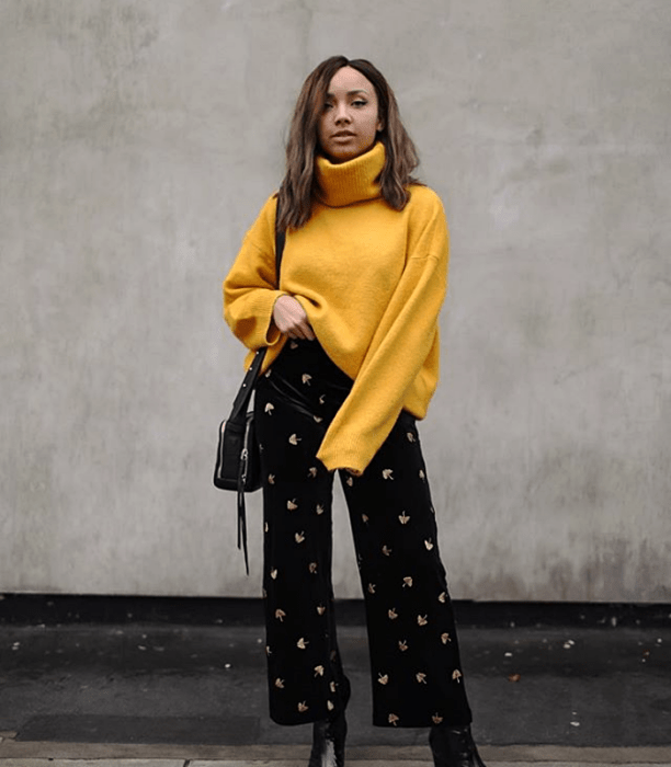 chica morena usando un suéter amarillo de cuello alto, pantalones acampanados de pana con estrellas y bolso de mano negro