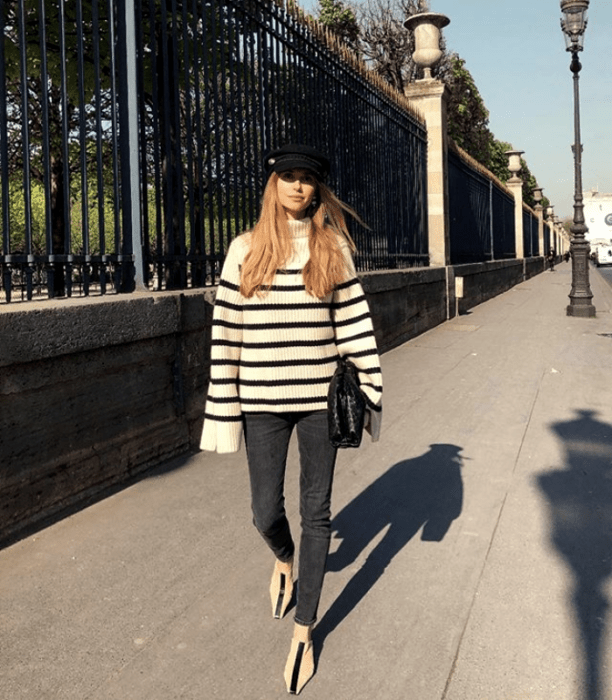 chica de cabello rubio usando un suéter de rayas blancas y negras, leggings y zapatillas de suelo con boina negra