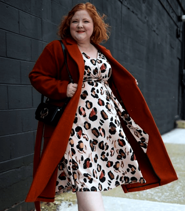 chica pelirroja curvy usando un abrigo naranja largo, bolso negro de piel y vestido midi de animal print