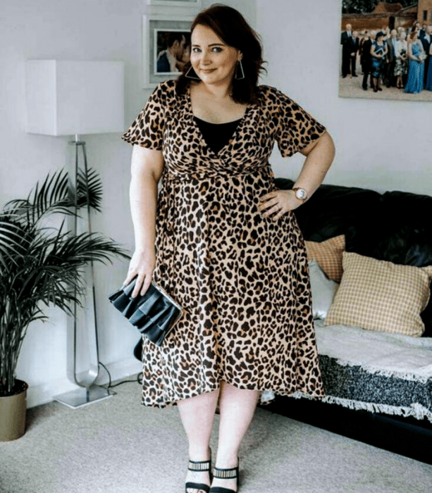 chica curvy de cabello castaño usando un vestido midi de animal print con cuello en v y manga corta, bolso de mano negro y sandalias de tacón negras