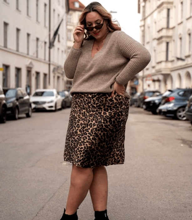 chica curvy usando lentes de sol, suéter café y falda midi de animal print con botines negros