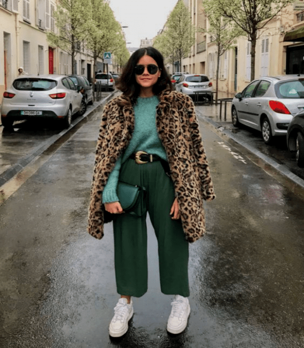 chica curvy de cabello castaño usando un suéter azul con abrigo de animal print, pantalones culotte verdes, tenis blancos y bolso verde de mano