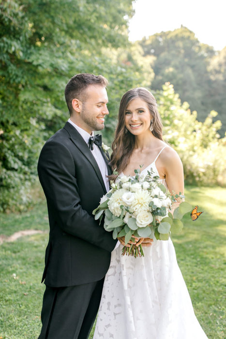 Pareja de novios posando para una sesión de fotos el día de su boda junto a una mariposa en un gran jardín 