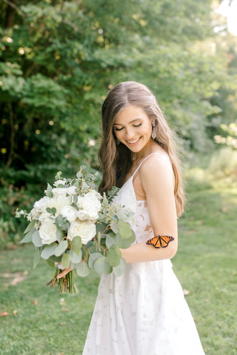 Novia sujetando su ramo mientras posa para una fotografía y una mariposa aparece cerca