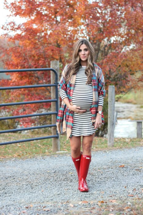 Chica usando un outfit de maternidad de vestido con rayas, botas de lluvia y poncho