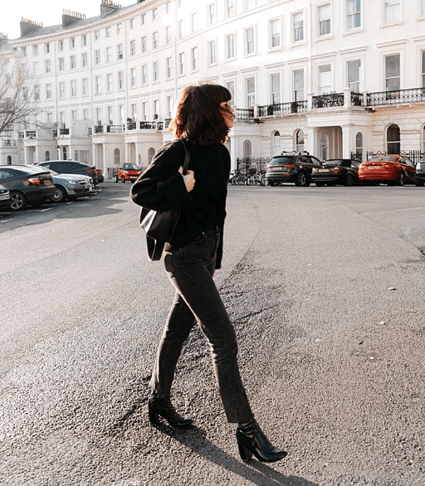 chica de cabello corto negro usando un suéter negro, bolso de mano negro, skinny jeans oscuros y botines de tacón de piel