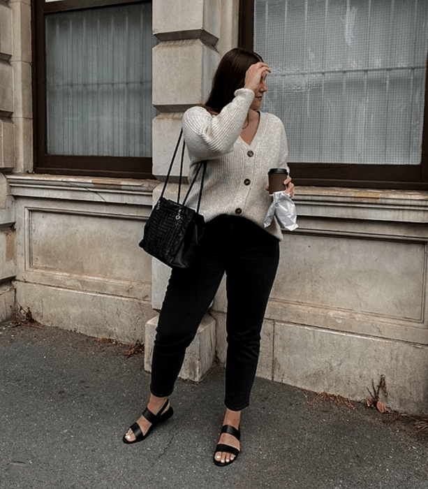 chica rubia usando un cárdigan blanco, skinny jeans negros, sandalias de piso negras y bolso pequeño negro