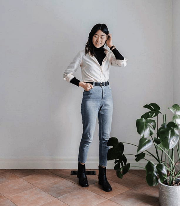 chica de cabello largo usando un top negro de cuello alto y una camisa blanca de botones, skinny jeans y botines negros