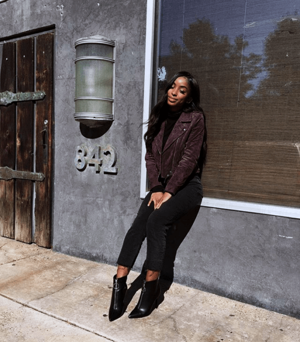 chica morena de cabello negro usando una chaqueta morada, top negro, skinny jeans oscuros y botines negros de piel