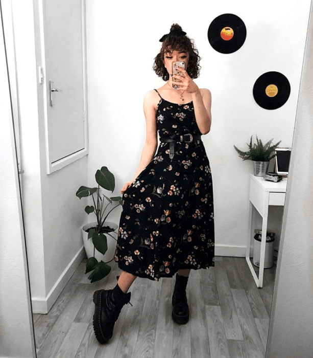 chica de cabello chino usando un vestido largo negro con flores, cinturón de cuero negro, botines negros de cuero sin tacón