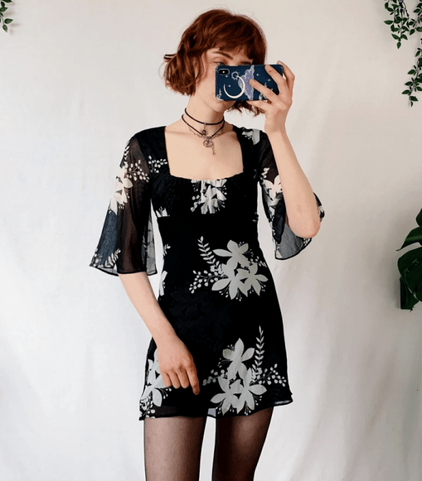 chica pelirroja usando un vestido mini negro con flores grises, manga 3/4 con medias negras