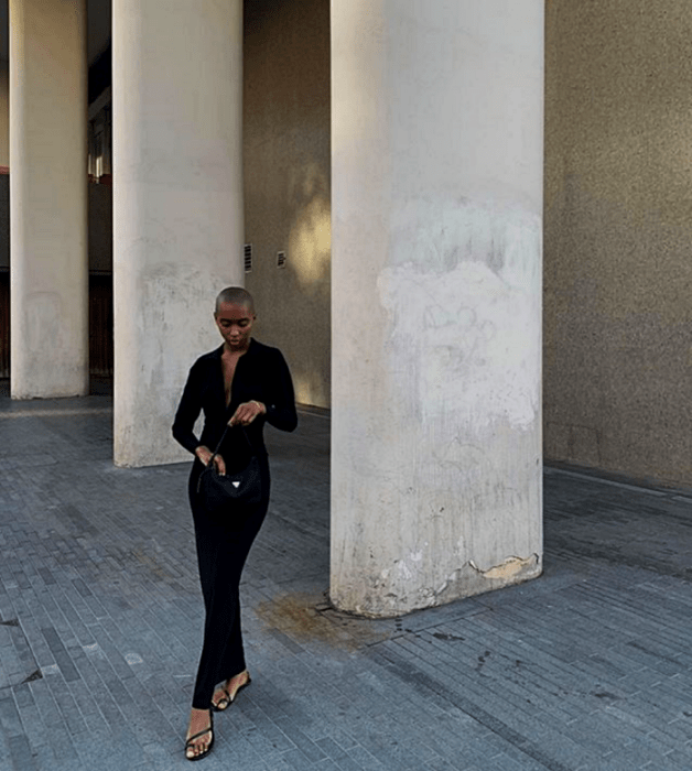 chica morena usando un vestido largo negro con cuello en V y sandalias negras de piso y bolso pequeño negro