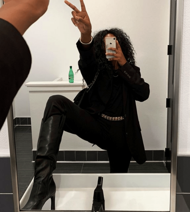 chica morena usando una camiseta negra, saco negro, pantalones negros de vestir, botas de tacón negras y bolso negro