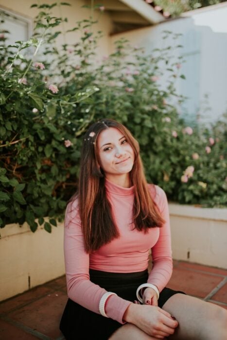 Chica con cuetér rosa sentada en un jardín