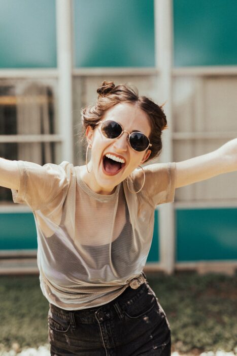 Chica con los brazos extendidos, usando gafas de sol y sonriendo