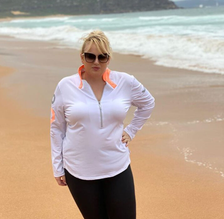 Rebel Wilson usando prendas deportivas y gafas de sol dando una caminata por la playa