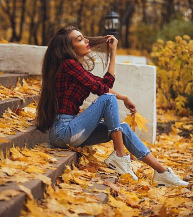 Chica sentada en unas escaleras donde está lleno de hojas de otoño